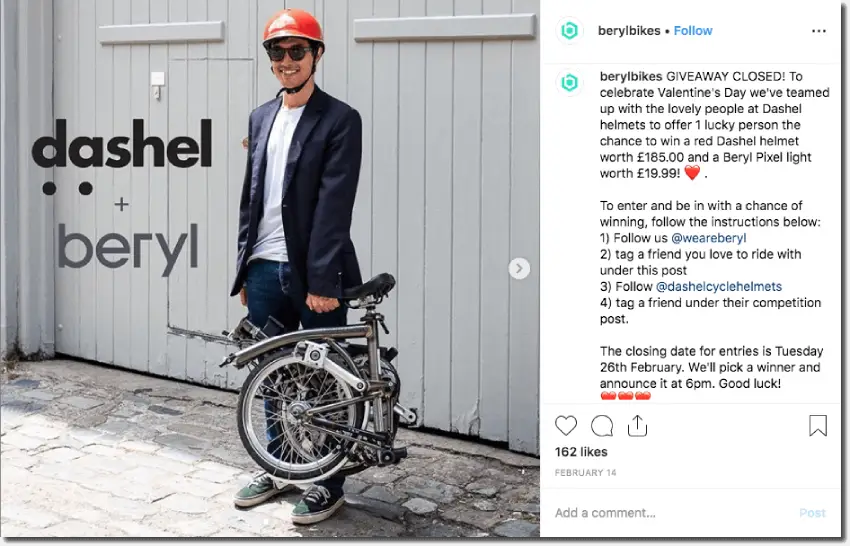 Screenshot of an Instagram giveaway by a cycling brand. The main image shows a casually-dressed young man, wearing a red helmet and sunglasses, and carrying a folding bike in one hand. The competition invites people to follow, comment, and tag for the chance to win a helmet and lights.