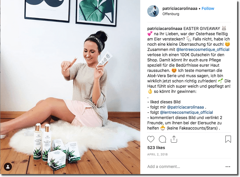 Example of an Easter giveaway on Instagram. The image shows a young woman sitting on a white fur rug in a room with white walls. At her feet, there are several make up products. She is holding a tube of moisturizer and applying it to her face.