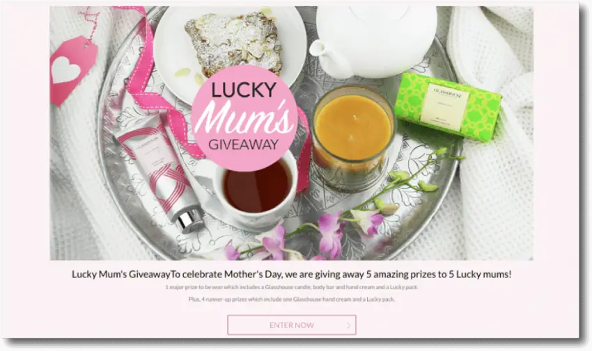 Banner announcing a Mother's Day giveaway. The image shows a breakfast tray with tea, candles, cake, a teapot, and luxury toiletries. The text below reads: "Lucky Mums Giveaway. To celebrate Mother's Day, we are giving away 5 amazing prizes to 5 lucky mums!"
